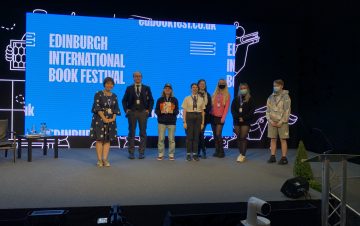 Image shows Prof Stella Chan and the young citizen scientists on stage at the book festival in front of a blue screen that says 'Edinburgh International Book Festival'